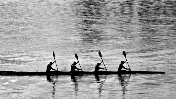 Four people paddling together in a long canoe, silhouetted against rippling water.