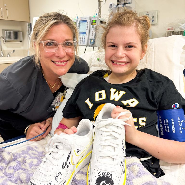 Gianna, and one of her Nurses Holly, smile with Nike shoes signed by the Iowa Football team 
